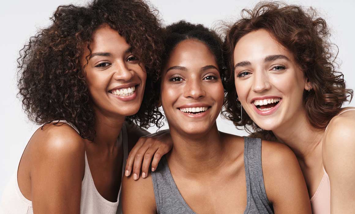 Three smiling young women with different skin types