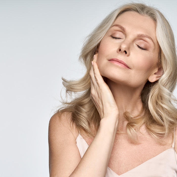 Mature woman with flawless skin holding hand to side of her face